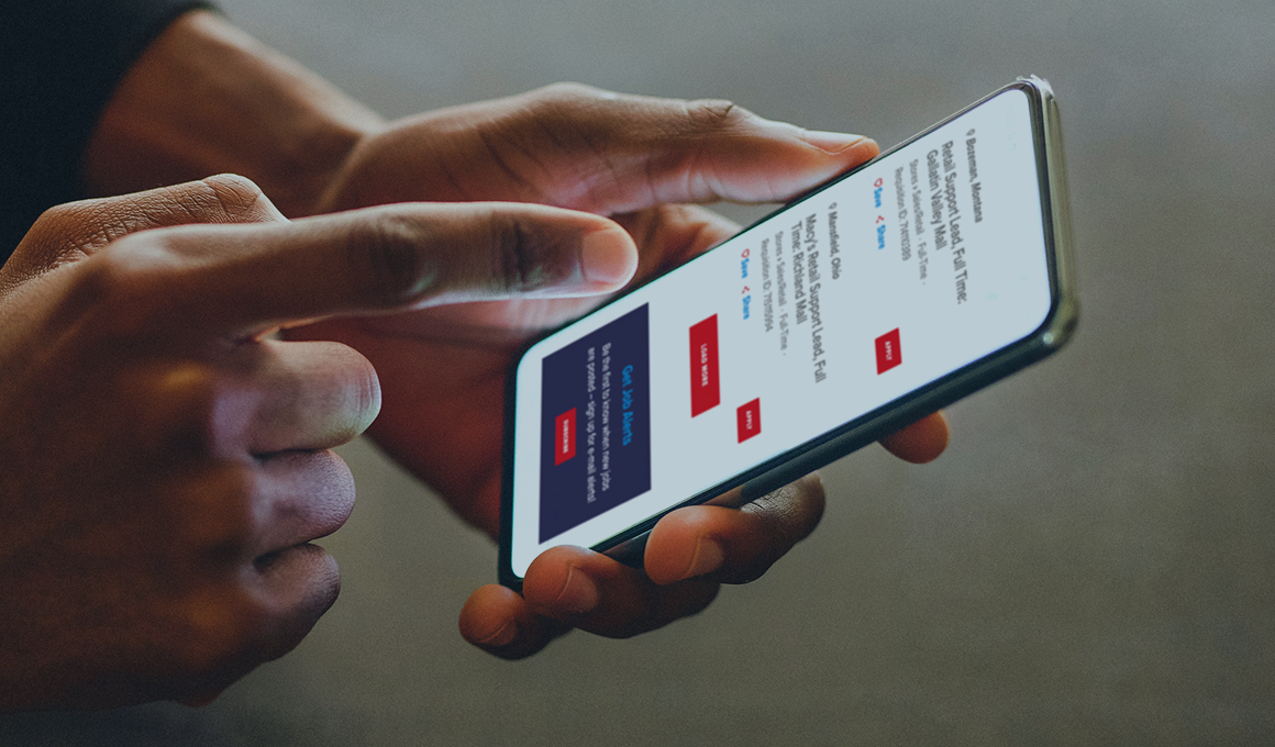 Close up of hands, one holding a smartphone and the other pointing at the screen that is showing job search results on the Macy's Jobs website.