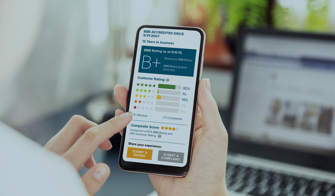A close up of hands, one holding a smartphone and the other pointing at the screen that is showing a business rating on the BBB website.